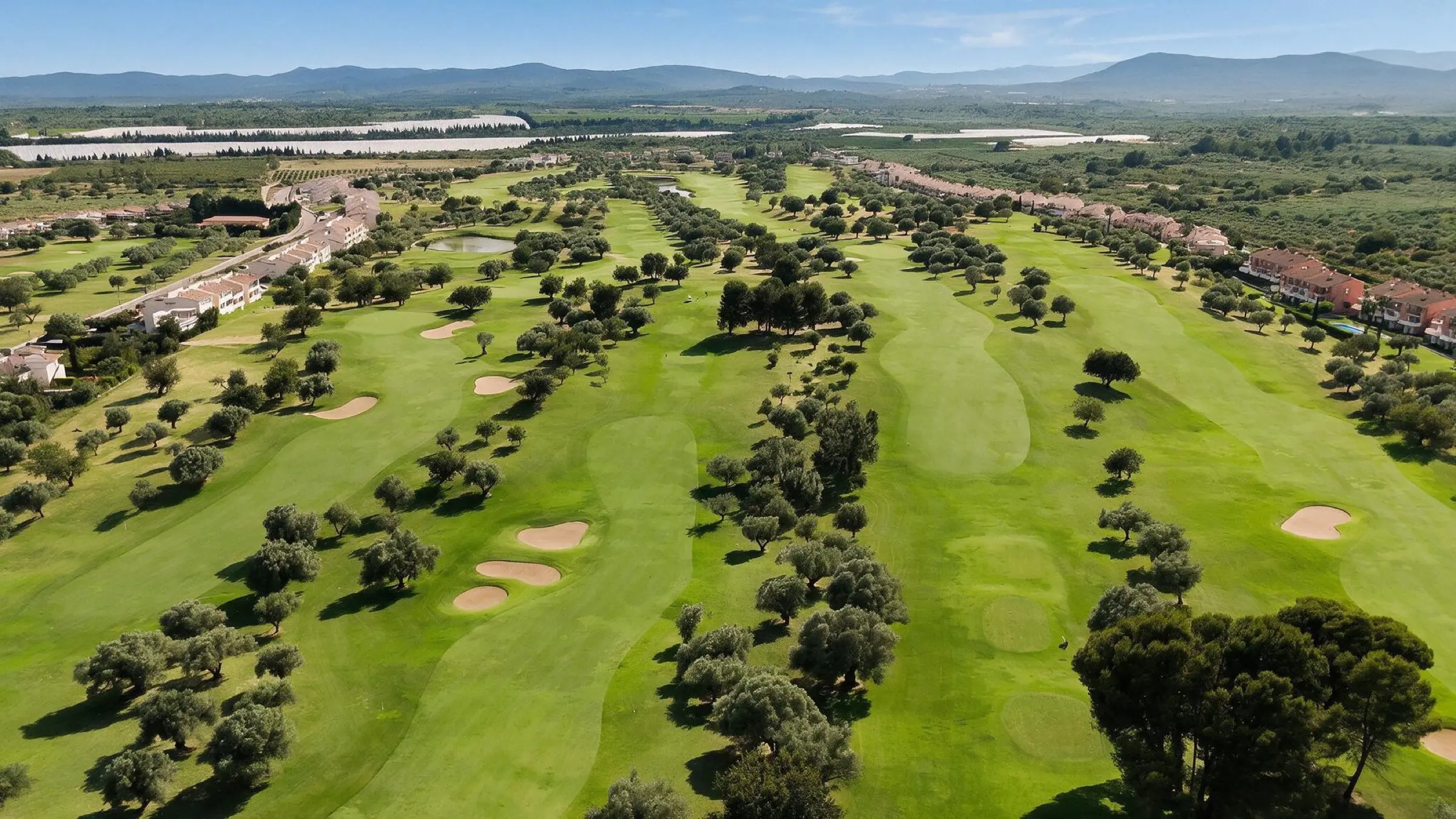 Vista aérea del campo de Panorámica Golf entre olivos, con las urbanizaciones a los lados y la sierra al fondo